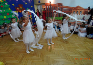 Na tle dekoracji światecznej dziewczynki tańczą z białymi szarfami.